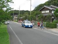 青色防犯パトロールと道路脇を歩く児童の写真