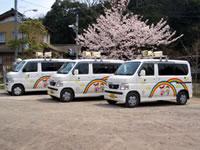 桜の木を背景に並ぶにこにこカーの写真